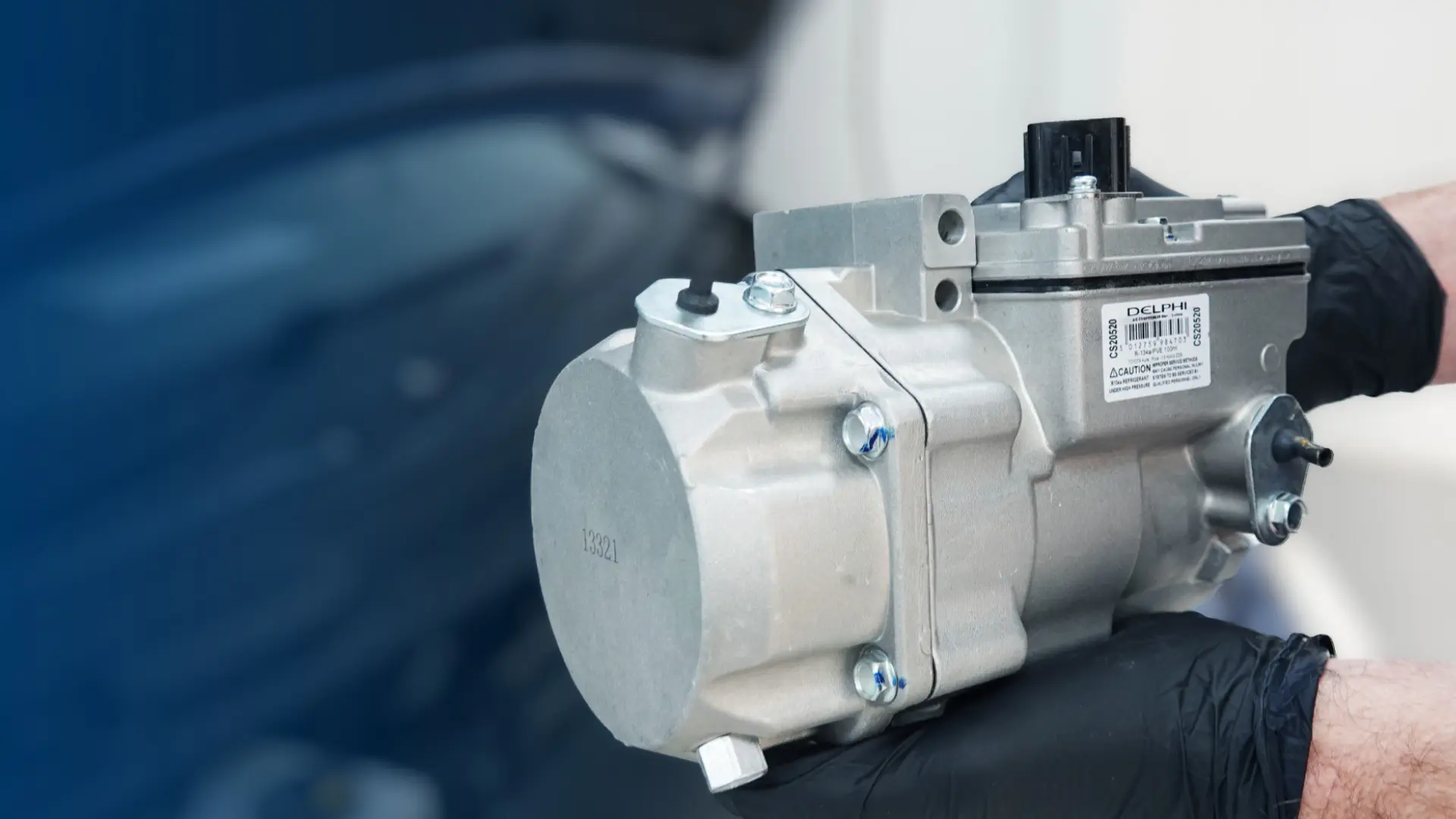 gloved mechanic hands holding a delphi automotive ac compressor unit for hvac diagnostics