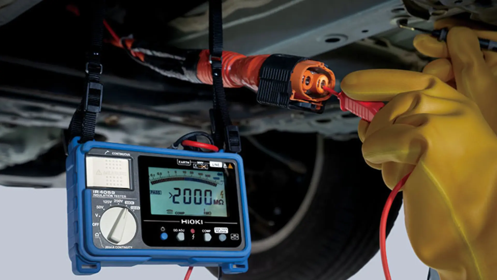 gloved technician using an insulation tester on an ev high-voltage cable under a vehicle