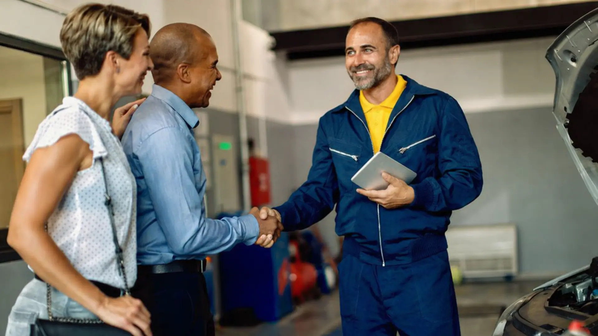 service advisor in uniform shaking hands with two customers next to a car with open hood