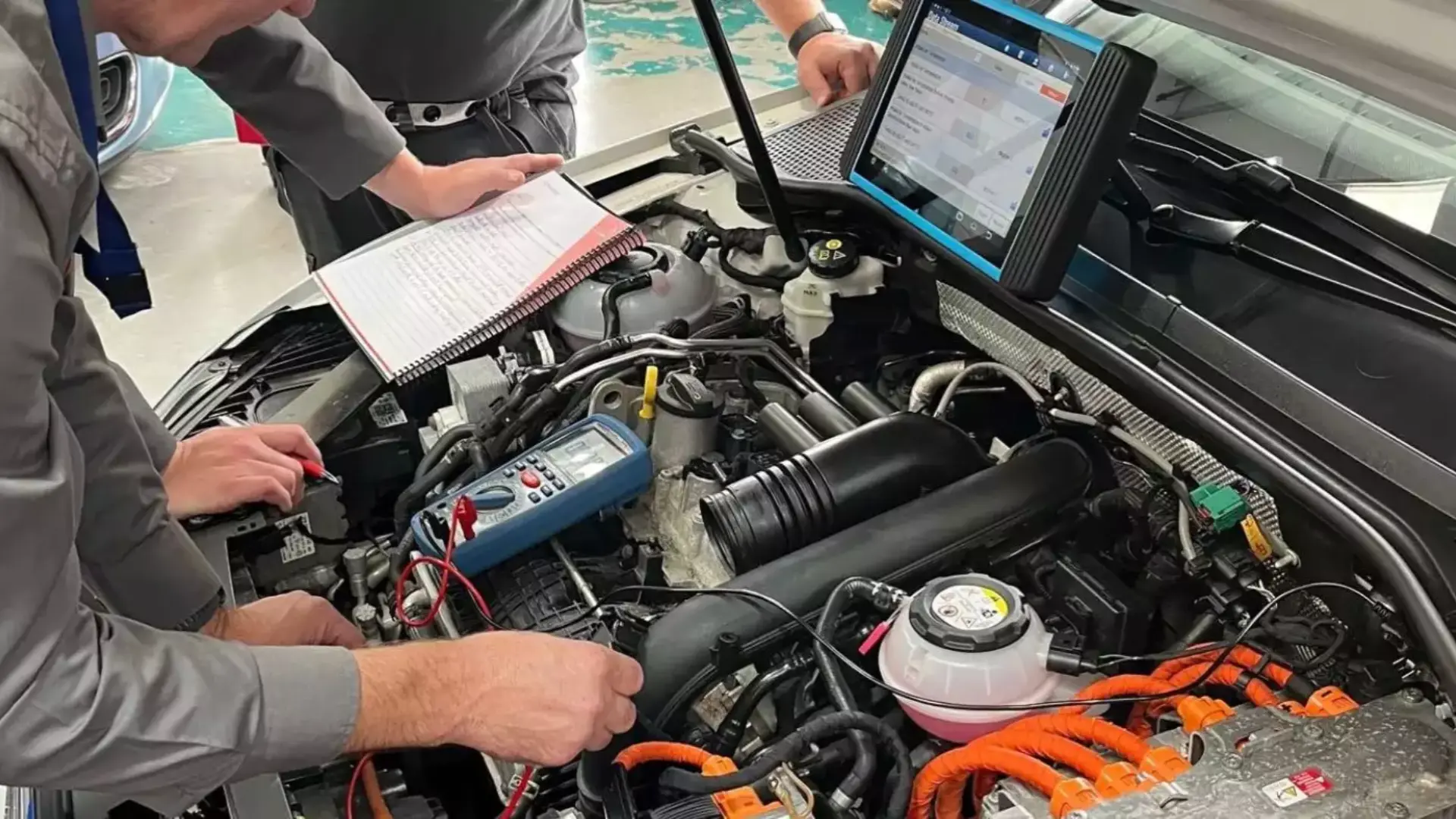 two ev technicians using a multimeter and diagnostic tablet to inspect an open engine bay
