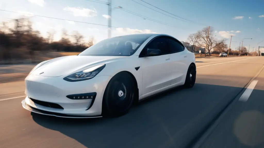 white tesla Model three in motion on an open road, highlighting its smooth aerodynamic curves and design